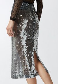 Silver sequin midi skirt with a side split, featuring a grid-like texture and shimmer effect. Material is lightweight with a form-fitting design.