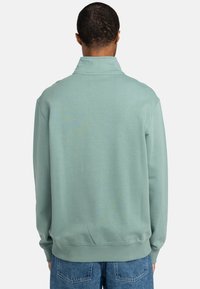 Light green pullover with a high collar, ribbed cuffs, and a relaxed fit. Smooth fabric with a subtle texture. No visible logos or branding.