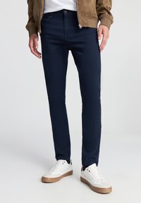 Granatowe bawełniane chinosy o dopasowanym kroju z bocznymi kieszeniami, w połączeniu z białymi trampkami z beżową podeszwą i czarnymi akcentami.