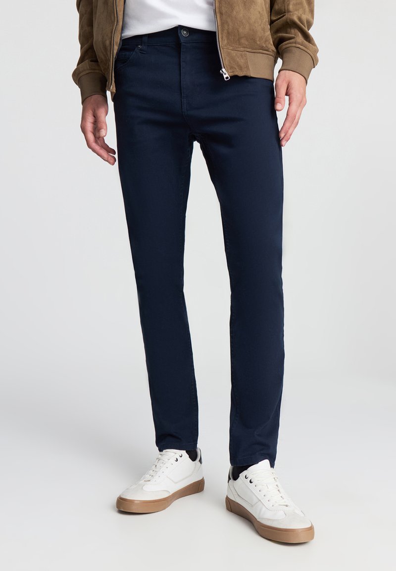 Granatowe bawełniane chinosy o dopasowanym kroju z bocznymi kieszeniami, w połączeniu z białymi trampkami z beżową podeszwą i czarnymi akcentami.