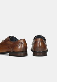 Pantofi de piele maro pentru bărbați, cu o textură netedă, având vârful rotund, design cu șireturi și toc jos, stratificat. Detalii de cusătură vizibile pe laterale.