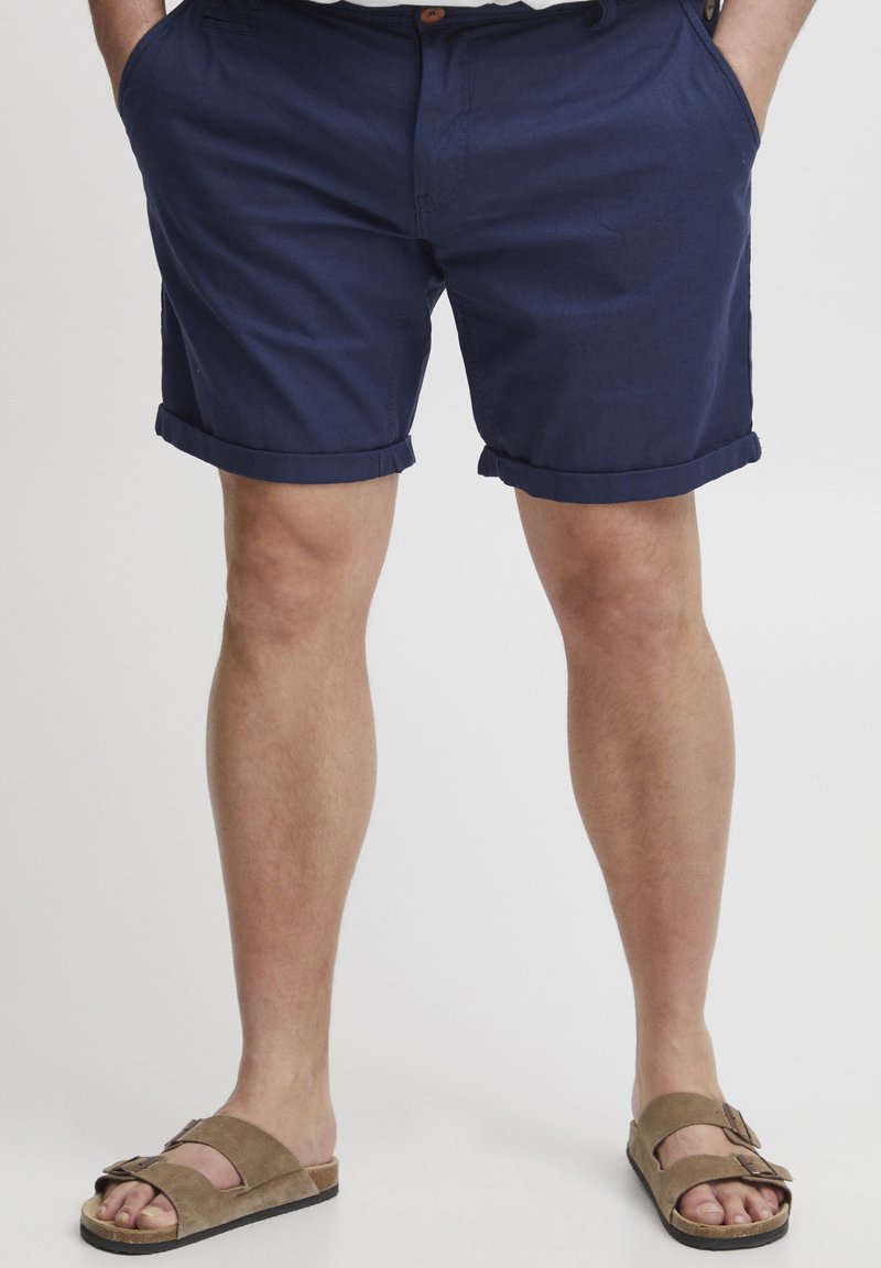 Mørkeblå bomullsshorts med rullet kant, sidelommer og knappelukking. Kombinert med brune semskede sandaler med justerbare stropper.
