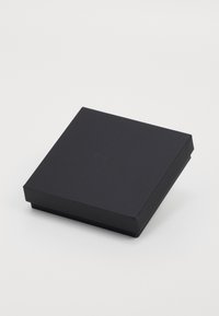 Melnas kvadrātveida dāvanu kaste ar nedaudz teksturētu virsmu un smalki iepresētu logotipu uz vāka, novietota uz baltā fona.