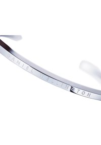 Hõbedane kell poleeritud metallrinnaga, mille siseküljel on graveeritud "DANIEL WELLINGTON", näidates sujuvat ja minimaliseeritud disaini.