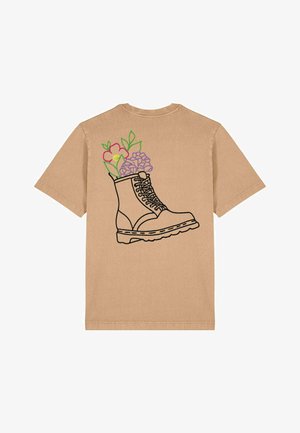 Korte mouwen t-shirt in tan met een ontwerp van een laars in zwart omtrek, met kleurrijke bloemembroidery in de laars en groene bladeren.