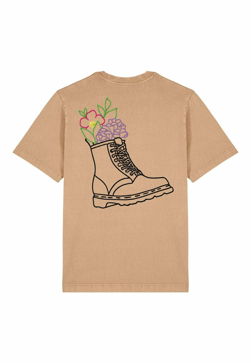 T-shirt à manches courtes beige avec un design de bottes en contour noir, orné de broderies florales colorées à l'intérieur des bottes et de feuilles vertes.