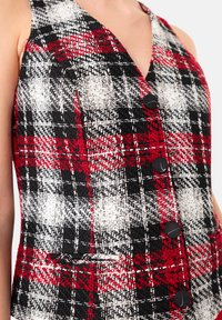 Rood, zwart en witte geruite vest met een V-hals, gestructureerde stof en vijf zwarte knopen aan de voorkant. Heeft een klein voorkantzakje.
