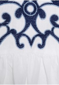 Tessuto bianco con raffinata ricamatura blu navy caratterizzata da motivi vorticosi e una textura arricciata lungo il bordo inferiore.