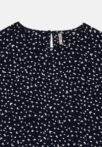 Blouse bleu marine en tissu léger avec un motif abstract de pois blancs. Fermeture à boutons à l'arrière avec un petit détail en trou de clé au niveau du cou.