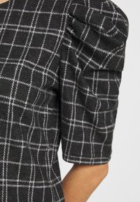 Top gris a cuadros con mangas cortas abullonadas, que presenta una tela texturizada y un patrón de rejilla blanca, destacando un diseño entallado.