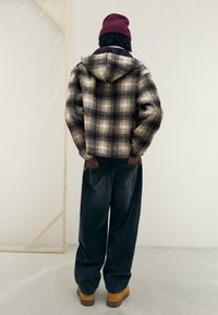 Brun och beige rutigt flanelljacka med huva, kombinerad med mörka manchesterbyxor och bruna stövlar. Texturerad tyg och avslappnad passform.