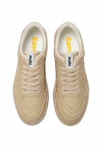 Bežīgi ādas sporta apavi ar saitēm, caurdurtām pirkstu daļām, baltu polsterētu iekšpusi un "MoEa" uzlīmi uz mēles, skatīti no augšas.