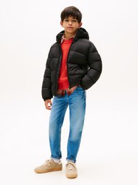 Doudoune noire avec capuche, pull rouge en laine, jeans bleu clair et baskets beiges avec lacets blancs. Chemise à carreaux simple en dessous.