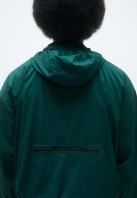 Grønn hettegenser med glatt tekstur, med en bakre glidelåslomme og elastiske ermer. Enkel, funksjonell design.