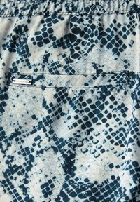 Blue and white patterned fabric featuring a snake-skin design. Includes a small, silver metal tag. Soft texture, lightweight material.