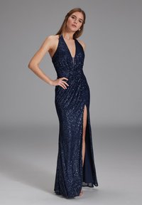 Meripik halter berwarna navy dengan leher V dalam, detail berkerut di pinggang, dan belahan tinggi di salah satu sisi. Siluet yang halus dan pas.