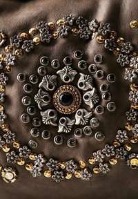 Accenti metallici decorativi su pelle scura; presenta fiori argentati, borchie dorate e argentate, design circolare con un gemma nera centrale.