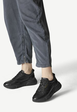 Baskets en cuir noir avec finition texturée et bout rond, dotées de lacets et d'une semelle noire épaisse. Portées avec un pantalon gris raccourci.
