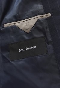 Interno di un blazer blu navy con finitura in raso e una tasca beige chiaro. È visibile un'etichetta nera con la scritta "Matinique" ricamata in bianco.