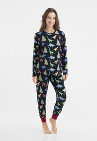 Pajama set s dlouhými rukávy s dinosaury na tmavě modrém pozadí, obsahující barevné dinosaury a vánoční stromečky, a červené manžety na kalhotách.