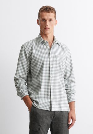 Chemise à carreaux verts et blancs, à manches longues, col boutonné, poche poitrine unique, en coton. Assortie avec un pantalon cargo gris.