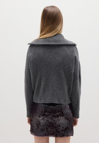Suéter de punto gris oscuro con un amplio cuello acanalado, combinado con una falda ceñida de lentejuelas. Contrastes de textura entre la tela de punto y las brillantes lentejuelas.