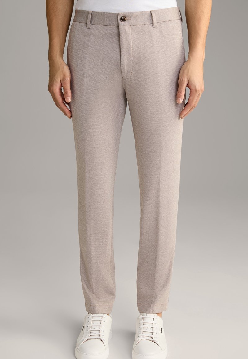 Ljusbeige byxor i texturerat tyg, skräddarsydd passform, med knappknäppning fram och sidofickor, kombinerat med vita sneakers.