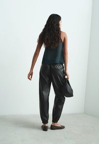 Crne kožne hlače suženog kroja, tamno zelena prozirna majica bez rukava, teksturirana crna torba i baletanke s ukrasnim zakovicama.