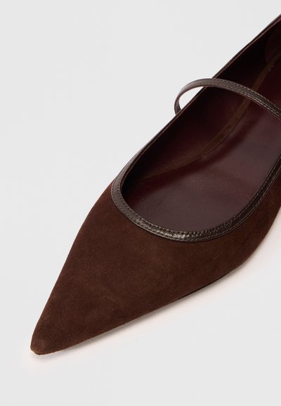 Chaussure plate en daim brun avec un bout pointu et une fine bordure métallique autour de l'ouverture. Doublure intérieure lisse.