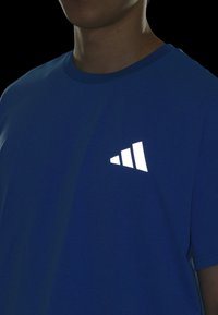 T-shirt in cotone blu concollo rotondo e maniche corte; presenta un logo triangolare bianco riflettente nella zona sinistra del petto.