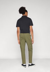 Černé polo tričko, olivově zelené cargo kalhoty s bočními kapsami a černé tenisky s bílou podrážkou. Hladký materiál a volný střih.