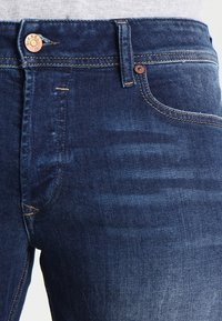 Mörkblå denimjeans med en lätt urtvättad textur, med knappstängning, kopparfärgade nitar och klassisk femfickdesign.