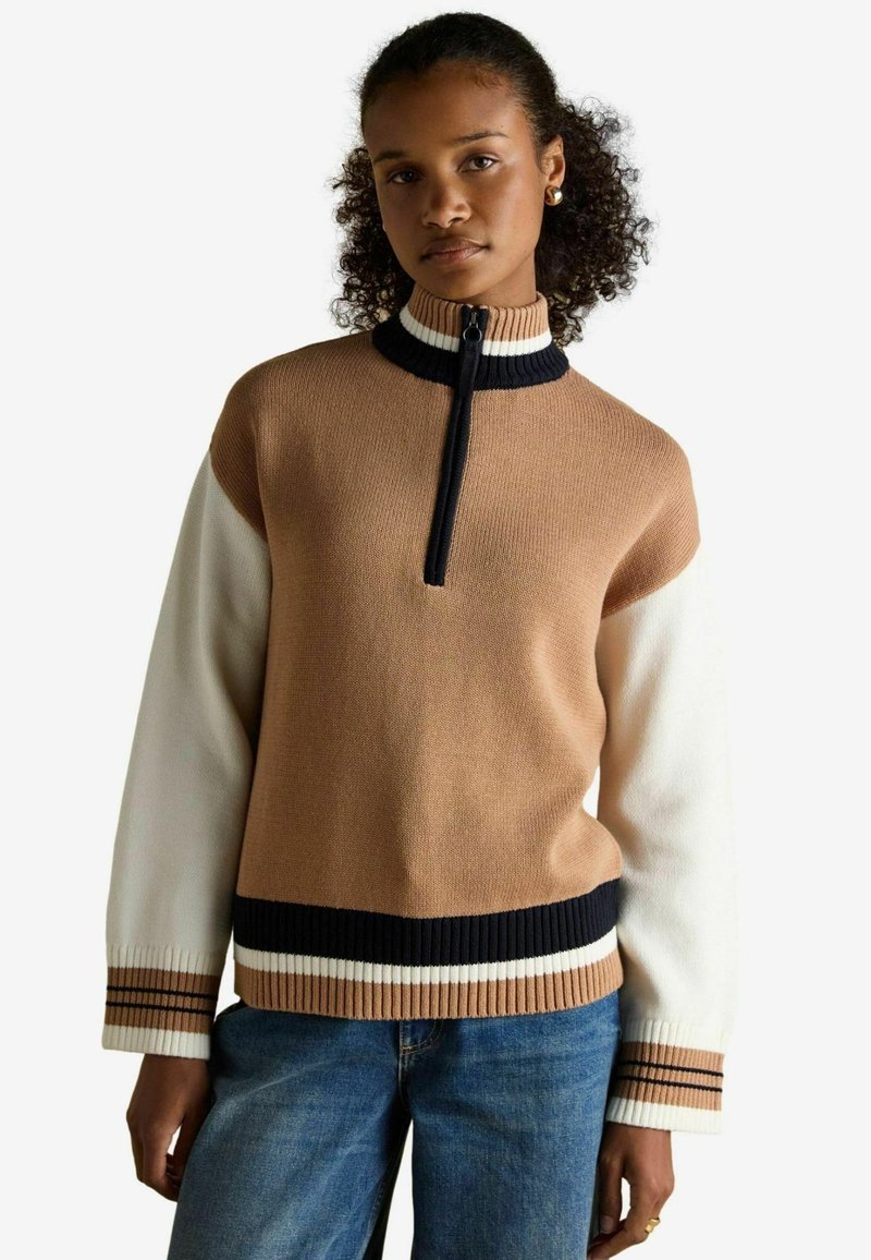 Pruun ja kreemikas sviiter, millel on tõmblukuga krae, mustad ja valged ribatekstuuriga detailid varrukatel ja servadel; pehme kudumise tekstuur.