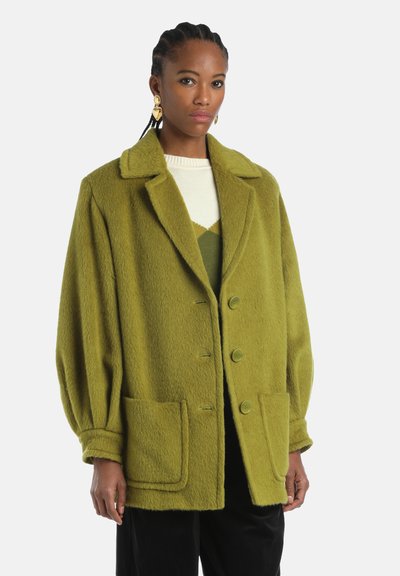 Groene wollen oversized jas met een reverskraag, drie grote knopen en twee opgestikte zakken. Heeft een gestructureerde stof en een ontspannen pasvorm.