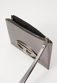 Clutch in finta pelle grigia con accenti in hardware argentato lucido e chiusura con zip. Presenta un cinturino da polso staccabile e una texture liscia.