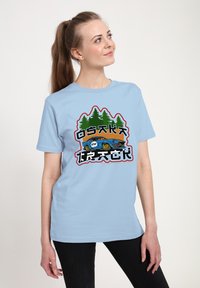 Světle modré bavlněné tričko s grafickým designem, na kterém jsou zelené stromy, stylizované auto a text "OSAKA" v černé a červené barvě.