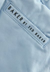 Jasnoniebieska tkanina o gładkiej fakturze z naszywką z napisem „BAKER by TED BAKER” w czarnym kolorze.