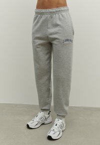 Jasnoszare dresy wykonane z mieszanki bawełny z elastycznym paskiem. Posiadają haftowane napisy "LAMANIA" w granatowym kolorze na lewej biodrze.