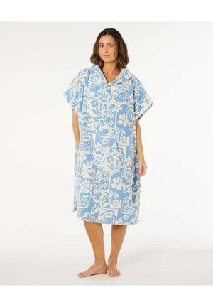 Kvinde står barfodet iført en blåt og hvidt blomsterprintet hættetrøjet poncho med en forlommer.