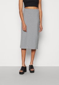 Svart och vit houndstooth midi kjol med en åtsittande silhuett, texturerad tyg och en slät midja, tillsammans med svarta blockklacksandaler.