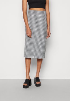 Schwarz-weißer Hahnentrittmuster-Midirock mit taillierter Silhouette, strukturiertem Stoff und glattem Bund, kombiniert mit schwarzen Blockabsatzsandalen.