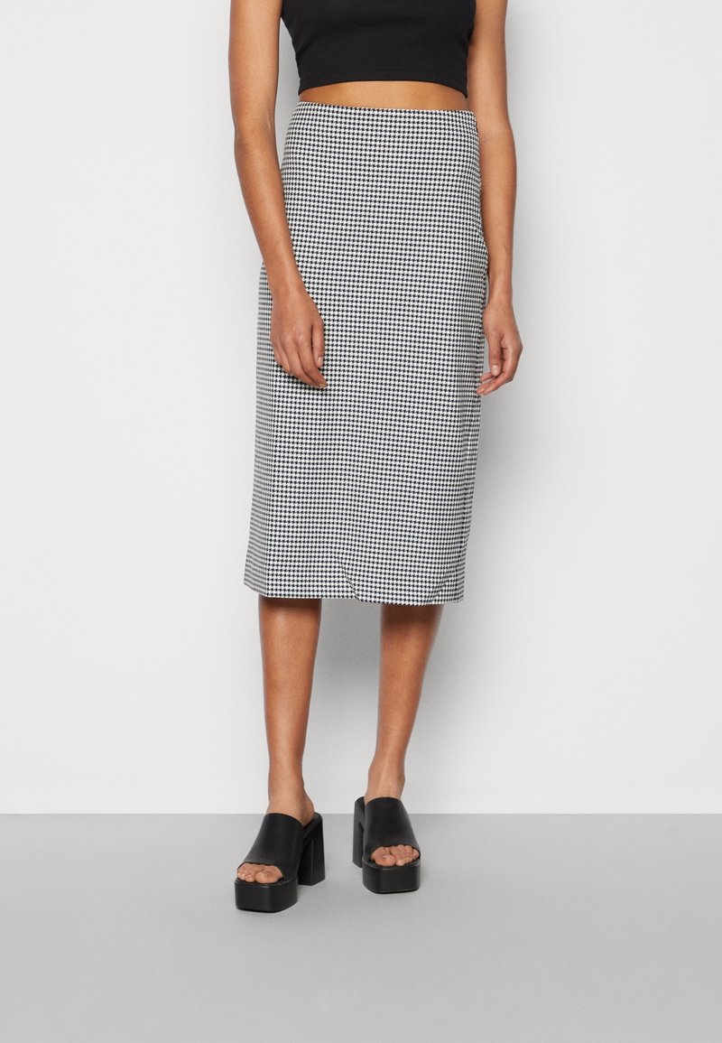 Svart och vit houndstooth midi kjol med en åtsittande silhuett, texturerad tyg och en slät midja, tillsammans med svarta blockklacksandaler.