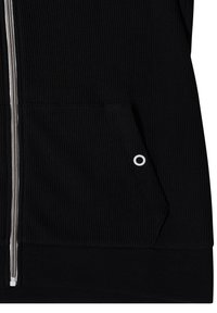Tissu noir texturé d'une veste avec une fermeture éclair à l'avant et une poche avec un petit détail circulaire blanc.
