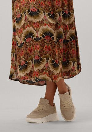 Beige suede sneakers with round toes, padded ankle collars, and thick white soles, paired with a floral patterned long dress in warm colors.