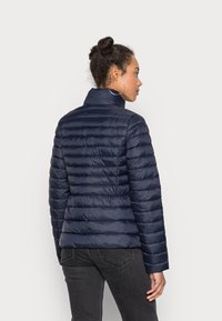 Giacca a vento blu navy con cuciture orizzontali, colletto alto e maniche lunghe. Presenta un design elegante, trapuntato per garantire calore.
