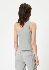Grijze, aangesloten, mouwloze top met een asymmetrische halslijn. Textuurstof, op maat gemaakte ontwerp en een gladde achterkant. Draagt bijpassende grijze broek.