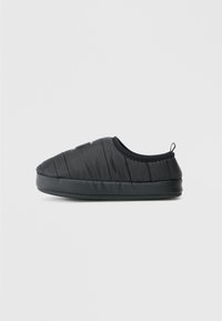 Zapatos negros tipo slip-on con parte superior de nailon acolchado, puntera redonda y suela de goma texturizada, con una pequeña lengüeta trasera para facilitar su uso.