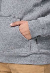 Felpa grigia con una texture morbida, dotata di tasca a marsupio e polsini a coste, abbinata a pantaloni beige.