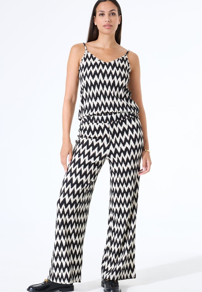 Conjunto de dos piezas en blanco y negro con patrón de zigzag, que incluye un top sin mangas de corte holgado y pantalones de pierna ancha, hechos de una tela ligera.
