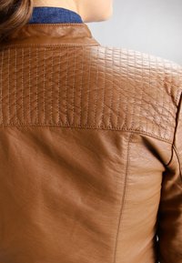 Vue arrière d'une personne portant une veste en cuir marron avec des coutures matelassées sur le haut du dos et un col bleu en dessous.